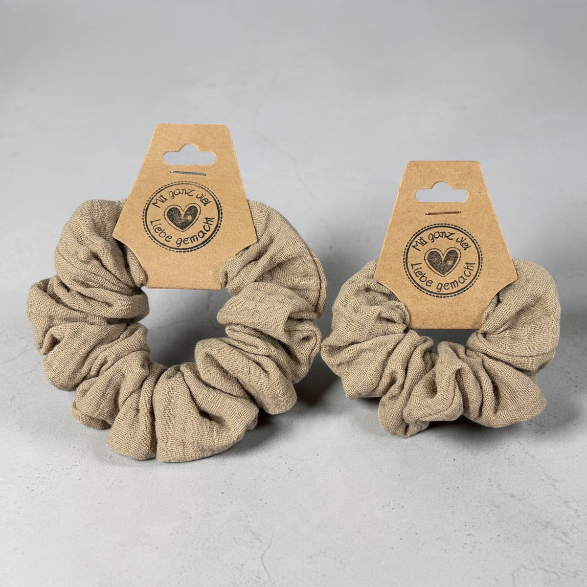 Zwei handgemachte Musselin-Scrunchies in Farbe Leinen, groß und klein nebeneinander zum Größenvergleich
