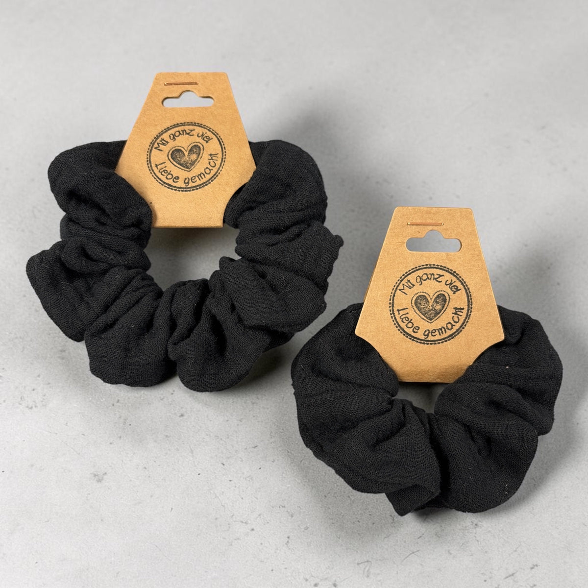 Zwei handgemachte schwarze Musselin-Scrunchies, groß links und klein rechts, zum Größenvergleich
