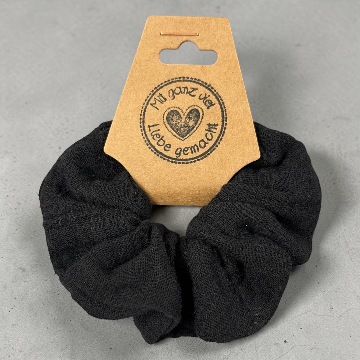 Kleiner handgemachter schwarzer Musselin-Scrunchie, ca. 8 cm Außendurchmesser, von oben mit Papieretikett
