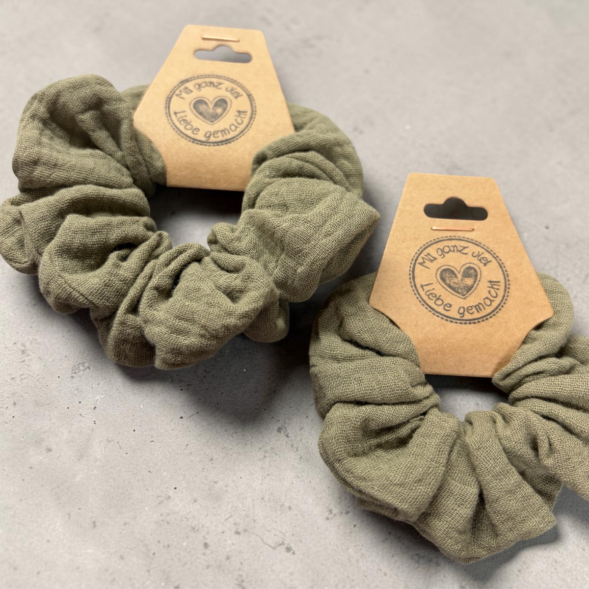 Großer und kleiner handgemachter Musselin-Scrunchie in Oliv, aus schräger Nahansicht mit sichtbarer Stoffstruktur
