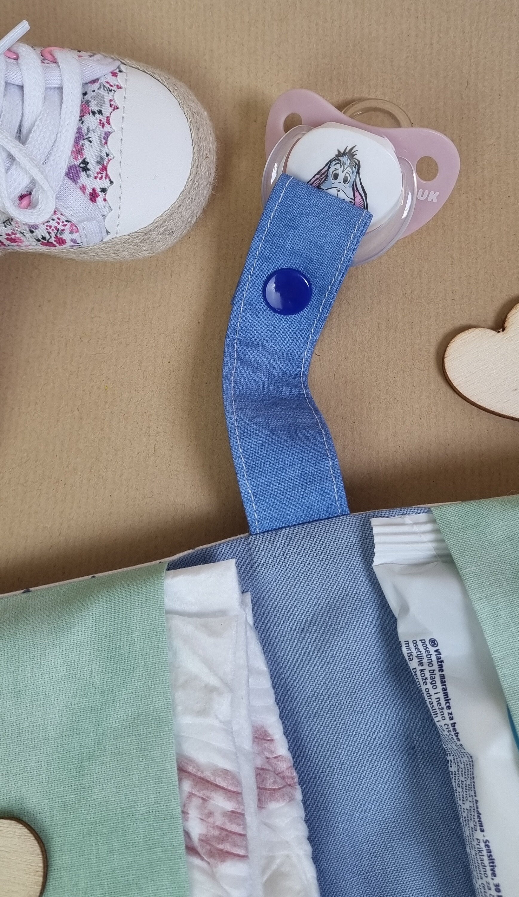 Handgemachte Windeltasche – Detailansicht Schnullerband mit blauem Druckknopf und geöffnete Fächer
