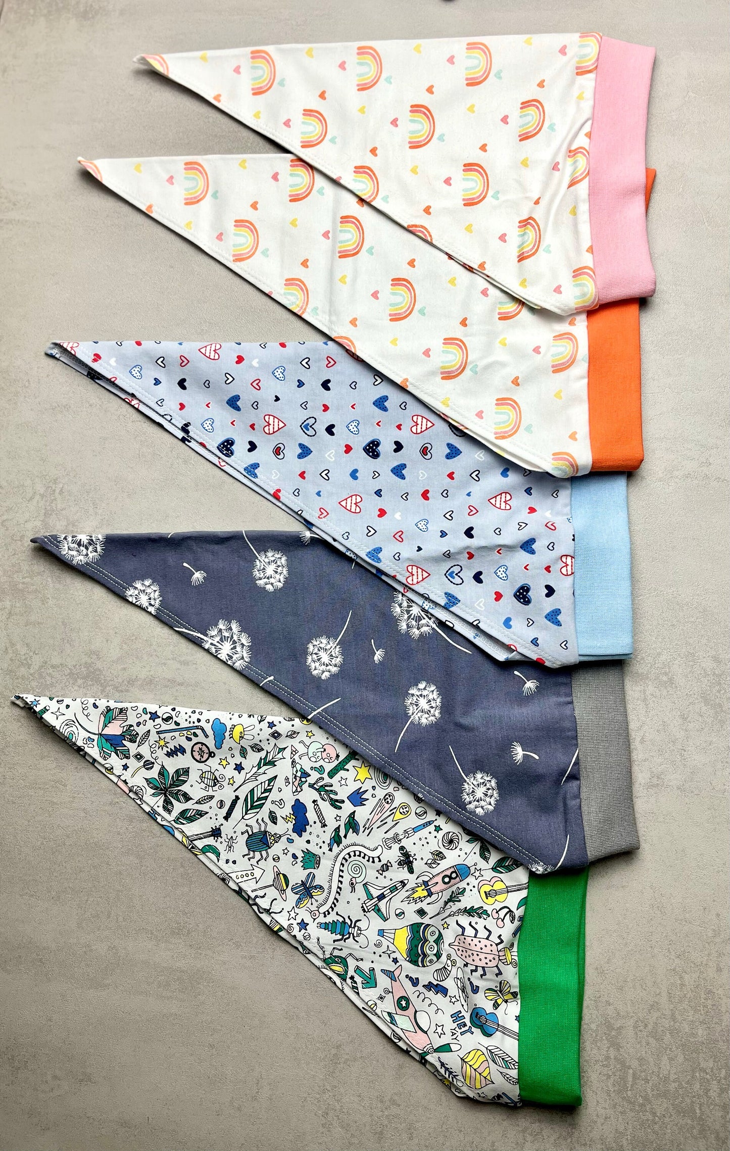 Handgemachtes Kinder Kopftuch mit Nackenschutz – alle 5 Muster seitlich übereinander: Regenbogen rosa, Regenbogen orange, Herzen blau, Pusteblume grau, Buntes Muster grün | OhMamaLina