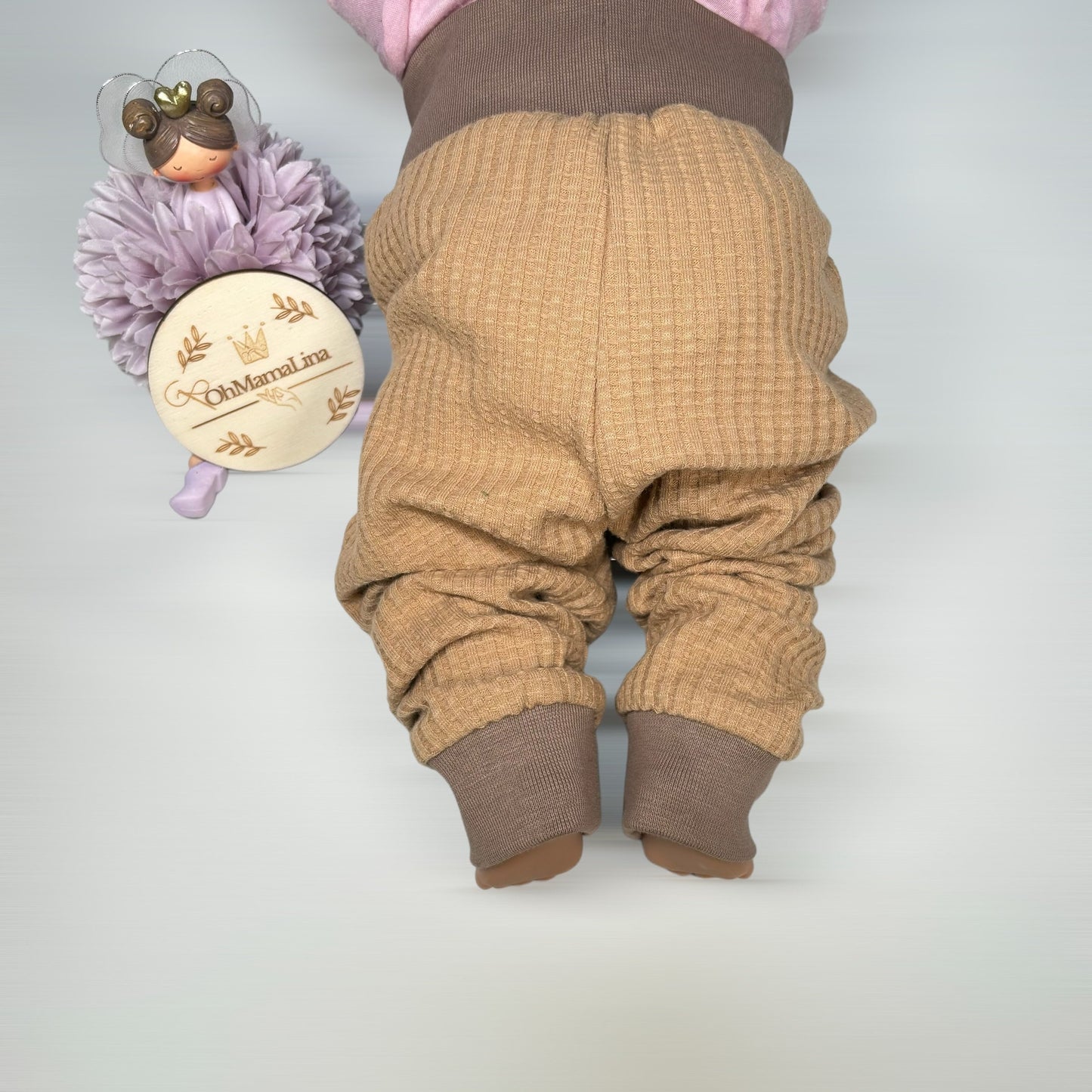 Handgemachte Kinderhose in Karamell aus Waffeljersey mit braunem Bündchen – Rückenansicht an Baby